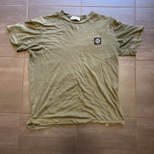 Stone Island  - Säljer en olivgrön t-shirt från Stone Island med en liten logga på bröstet. T-shirten har en klassisk rund hals och korta ärmar. Perfekt för en avslappnad stil.