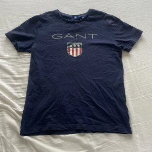 Gant T-shirt - Snygg mörkblå t-shirt från GANT med ett stilrent tryck av märkesnamnet och en sköld med stjärnor och ränder på framsidan. Perfekt för en avslappnad stil.