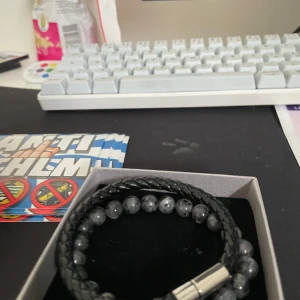 Svart och grått armband - Snyggt set med två armband. Ett flätat svart läderarmband med silverfärgat magnetlås och ett elastiskt armband med grå pärlor. Perfekt för att ge en stilren touch till din outfit.