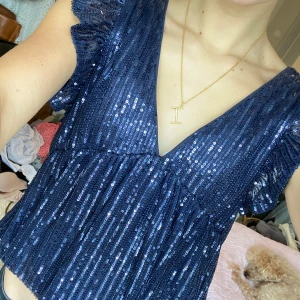 Mörkblå glittrig topp från Nelly  - Säljer en snygg mörkblå paljett topp med v-ringning och volangdetaljer. Toppen är perfekt för festliga tillfällen. Endast använd 1 gång💓😊