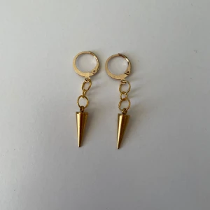 Guldiga örhängen med konformad hängande detalj - Säljer ett par handgjorda guldörhängen. Rostfritt material och nickelfria.
