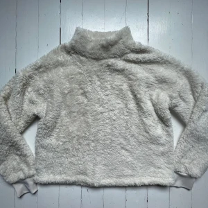 Vit fluffig fleece-tröja från SOC - Supermjuk och varm vit fleece-tröja från SOC med hög krage. Perfekt för kyliga dagar. Tröjan har långa ärmar och muddar vid ärmslut och nederkant. Snygg och enkel att matcha med det mesta.