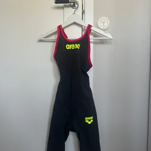 Svart tävlingsbaddräkt från Arena med rosa detaljer - Tävlingsbaddräkt från arena. Använd men fortfarande i bra skick. Baddräkten är i storlek UK 26 (se bild). Säljes då jag slutat simma. Pris ligger på 1000 kronor. 