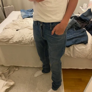 Blå jeans från Nudie Jeans Grim Tim - Säljer ett par klassiska blå jeans från Nudie Jeans i storlek w32/l32. Jeansen har en rak passform och normal midja, med snygga detaljer i kopparfärgade nitar och knappar. Perfekta för dig som gillar stilrena och tidlösa jeans.
