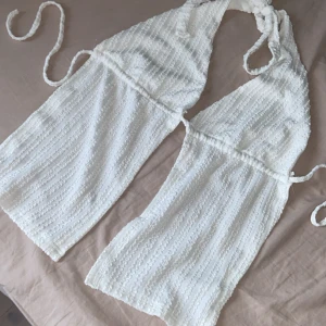 Vit omlottklänning med knyt från SHEIN - Säljer en vit omlottklänning från SHEIN i storlek S. Klänningen har halterneck med knyt i nacken och midjan, samt ett diskret randigt mönster i tyget. Perfekt för sommarens alla tillfällen!