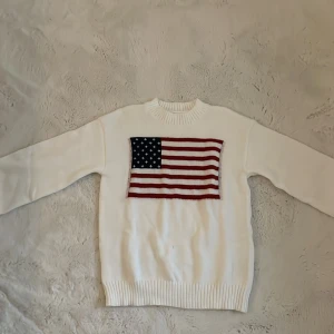 Vit stickad tröja med amerikansk flagga - Säljer en vit stickad tröja från temu med en stor amerikansk flagga broderad på bröstet. Tröjan har rund halsringning, långa ärmar och ribbade muddar vid ärmslut och nederkant. Perfekt för dig som gillar klassisk och preppy stil.