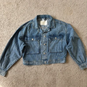 Ny jeansjacka - Säljer en klassisk blå croppad jeansjacka från & Denim. I storlek S. Kommer tyvärr inte till användning, helt ny och oanvänd. Har legat viken ett tag så kan behöva strykas. 