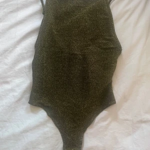 Glittrig baddräkt från Gina Tricot - Säljer en snygg glittrig baddräkt från Gina Tricot i storlek XS. Bodyn har smala axelband och en öppen rygg. Perfekt för dig som vill sticka ut på nattklubben 