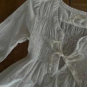 Odd Molly Blus - Superfin vit blus med smockdetaljer och knyt framtill. Vida trekvart ärmar med lätt volang vid ärmslut. Perfekt till sommaren och mycket bra skick!