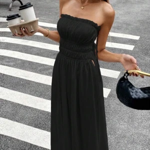 Svart axelbandslös långklänning med knyt - Säljer en svart axelbandslös långklänning med smockad överdel och knytdetaljer i midjan. Klänningen har en luftig passform och är perfekt för varma dagar. Enkel och stilren design som passar till många tillfällen.