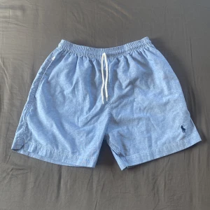Ljusblå shorts från Polo Ralph Lauren - Säljer ett par ljusblå shorts från Polo Ralph Lauren med vit snörning i midjan och broderad logga på ena benet. Shortsen har elastisk midja och en bakficka. Perfekta för sommardagar! Pris kan gå ner vid snabb affär, vid minsta lilla fråga är de bara att höra av dig. Mvh Oliver 