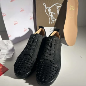 Svarta sneakers med nitar från Christian Louboutin (Eller byte) - Snygga svarta sneakers från Christian Louboutin med coola nitar på ovandelen. Skorna har en klassisk snörning och är tillverkade i skinn. Perfekta för att ge din outfit en edgy touch. Kan diskutera pris.(43)
