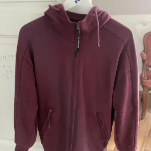 Cp company hoodie  - Säljer en vinröd hoodie från C.P. Company med hel dragkedja, huva och ikoniska goggles i huvan. Jackan har två fickor med dragkedja och är perfekt för dig som gillar streetwear och snygga detaljer. Skriv om ni har frågor eller funderingar, skick 9,5/10. 