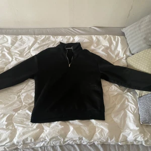 Svart tröja med dragkedja i halsen - Säljer en svart långärmad tröja med halv dragkedja i halsen. Perfekt för en stilren och enkel look. Tröjan har en hög krage och är i ett mjukt material.