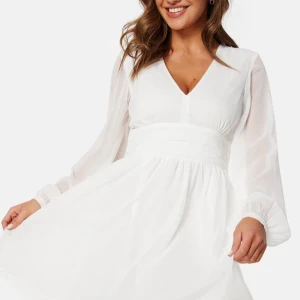 Vit långärmad klänning från Bubbleroom - Superfin vit klänning från Bubbleroom med v-ringning, markerad midja och långa, transparenta ärmar. Klänningen har knytband i ryggen och ett lätt tyg perfekt till sommaren. Klänningen är helt oanvänd och perfekt till student eller konfirmation