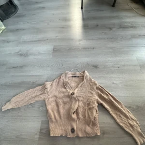 Beige stickad kofta från 157 - Säljer en beige stickad kofta från 157 i storlek S. Koftan har långa ärmar, v-ringning och knäpps med stora knappar framtill. Perfekt för lager-på-lager och enkel att matcha med olika outfits.