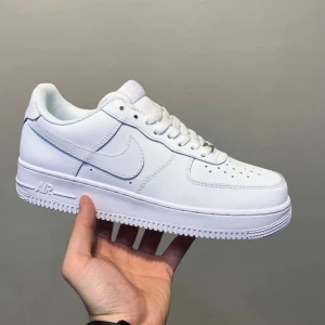 Nike Air Force 1 vita sneakers - Klassiska vita Nike Air Force 1 sneakers med låg profil och rund tå. Skon har snörning och är tillverkad i skinn med en platt sula. Perfekt för dig som gillar stilrena och tidlösa sneakers.