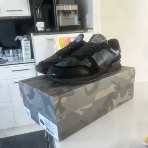 Valentino Garavani sneakers med camouflage - Säljer ett par snygga Valentino Garavani sneakers med svart och blått camouflage-mönster. Skorna kommer inte längre t användning så tänkte sälja dom för att bli av med dom. Där av det billiga priset. 