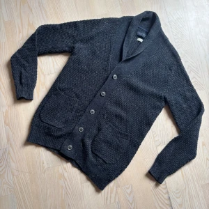 Stickad Kofta med Fickor - En skön mörk-blå/grå kofta med unik ribbing/ stickning. Finns två användbara fickor på koftan. Perfekt inför våren och sommaren! Storlek S men lutar lite åt M. Om ni har frågor eller funderingar om passform eller annat är det bara att höra av sig!