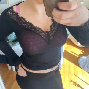 Svart långärmad blus med spetsdetaljer - Säljer en ultralätt svart långärmad blus i modalkashmir med vacker spets vid halsringning och ärmslut. Blusen är figurnära och har en elegant, transparent känsla. Perfekt för dig som gillar stilrena och feminina detaljer.