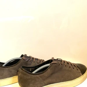 Bruna lanvin sneakers med svart tå - Säljer ett par stilrena lanvin sneakers i brun mocka med svart tå och svart sula. Skorna har snörning och en klassisk rund tå. Perfekta för dig som gillar en clean och tidlös look.