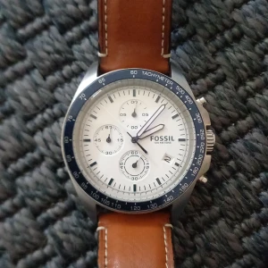 Fossil kronograf herrklocka med brunt läderband - Stilren herrklocka från Fossil med vit urtavla, blå bezel och brunt läderarmband. Klockan har kronograf-funktion, datumvisning och silverfärgat boett. Perfekt accessoar för dig som gillar klassisk design.