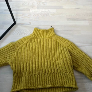 Gul ribbstickad polotröja från H&M - Säljer en gul ribbstickad polotröja från H&M. Tröjan har hög krage och långa ärmar, perfekt för kyligare dagar. Den är mjuk och har en oversized passform som ger en avslappnad look.