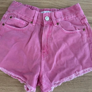 Rosa jeansshorts från Zara - Snygga rosa jeansshorts från Zara med fransig kant nertill och klassisk femficksdesign. Shortsen har bälteshällor och knappstängning framtill. Perfekta för varma dagar när du vill ha en färgklick i din outfit.