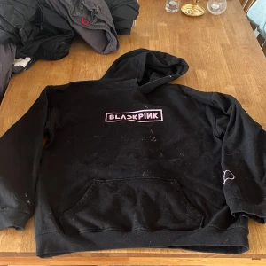 Svart BLACKPINK hoodie med tryck - Svart hoodie med rosa BLACKPINK-logga på bröstet, långa ärmar och huva. Använd många gånger, finns en fläck och tecken på användning.