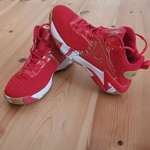 Röda sneakers med guldiga detaljer - Oanvända, snygga röda sneakers med coola guldiga detaljer och vit sula. Skorna har snörning och mönstrad yttersula för extra grepp. Perfekta för dig som vill sticka ut med färg och stil. Sportig design med modern känsla.