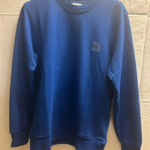 Blå sweatshirt från Stone Island - Snygg blå sweatshirt från Stone Island med rund hals och klassisk logopatch på bröstet. Tröjan har långa ärmar och ribbade muddar vid ärmslut och nederkant. Perfekt för dig som gillar stilren streetwear.