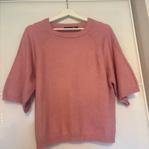 Rosa stickad tröja från 157, S - Mysig rosa stickad tröja från 157 med rund halsringning och halvlånga ärmar. Tröjan har en relaxed passform och ribbade muddar vid hals, ärmslut och nederkant. Perfekt för lager-på-lager och chill vardagsstil.