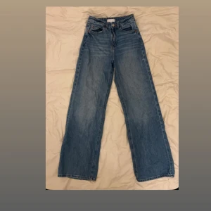 Blåa wide jeans med hög midja - Säljer ett par klassiska blå jeans storlek 164. Byxorna är i bra skick och har en avslappnad passform som passar till många olika outfits. Med lite vitt nagellack på sidan av benet.