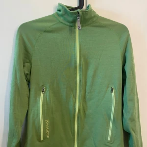 Grön hoddie med dragkedja  - Grön mikrofleecetröja från Houdini. Storlek M.