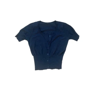 Svart kortärmad kofta med knappar - Kortärmad svart kofta med rund halsringning och knäppning framtill. Modellen är croppad och har bred ribbad midja som ger en snygg siluett. Perfekt att slänga över ett linne eller klänning för en chill look.