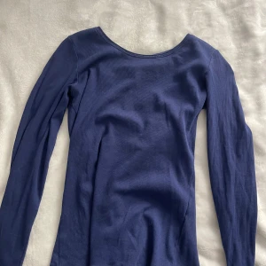 Mörkblå långärmad ribbad tröja - En enkel och stilren mörkblå långärmad tröja i ribbad bomull. Tröjan har en rundad halsringning och sitter tajt mot kroppen, perfekt för lager-på-lager eller som den är. Passar dig som gillar basic men ändå vill ha något snyggt.