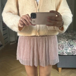 Plisserad glittrig rosa minikjol - Superfin plisserad kortkjol i ljusrosa med glittrigt tyg. Kjolen har elastisk midja och ett flowy fall som ger en riktigt söt och trendig vibe. Perfekt för dig som vill sticka ut lite extra med en touch av glitter.