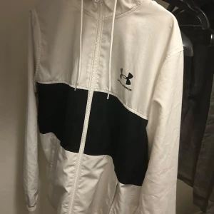 Vit under armour vindjacka - Säljer en vit ua vindjacka i vädligt bra skick. Den är i storlek M. Pytte lite smutsig vid armen
