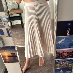 Plisserad långkjol i ljus beige - Säljer en superfin plisserad långkjol i ljus beige. Kjolen har ett brett resårband i midjan och faller snyggt med sina mjuka veck. Perfekt för dig som gillar en stilren och luftig look.