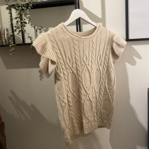 Beige stickad tröja med kort ärm - Säljer en beige stickad tröja med korta, voluminösa ärmar och snyggt flätmönster. Passar dig som gillar en mysig och trendig look. Tröjan är endast testad så den är inte använd! Stolek S