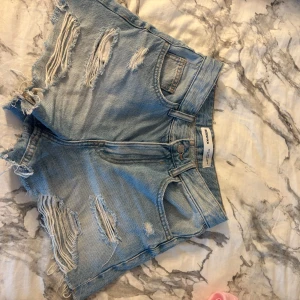 Ljusa jeansshorts från Bershka - Snygga ljusblå jeansshorts från Bershka med slitna detaljer och fransig kant. Klassisk femficksmodell med hög midja och dragkedja. .