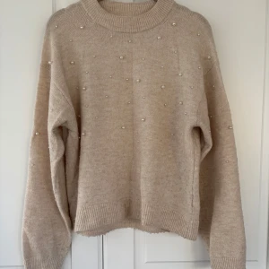 Beige stickad tröja med pärlor - Superfin beige stickad tröja med pärldetaljer över hela framsidan och ärmarna. Tröjan har en rund halsringning, ribbade muddar och en loose passform. Perfekt för dig som gillar en mysig och trendig look med lite extra bling. Från HM.