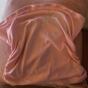 Rosa tubtopp med stjärnor  - Säljer en söt rosa tubtopp dekorerad med flera stjärnor i glittrande strass framtill. Perfekt för dig som gillar att sticka ut och vill ha något extra till outfiten. Mjuk och skön känsla, passar perfekt till sommarens varma dagar.