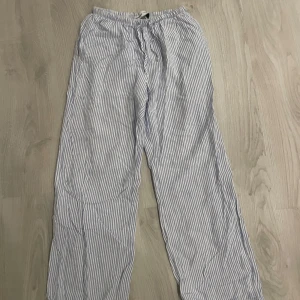 Randiga linnebyxor med snörning - Luftiga och sköna linnebyxor med blåvita ränder och snörning i midjan. Perfekta för varma dagar och chill vibes. Rak passform och elastisk midja för extra komfort.