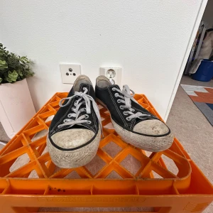 Svarta Converse All Star sneakers - Klassiska svarta Converse All Star sneakers med vit sula och tå, vita snören och tydliga kontrastsömmar. Låg modell med rund tå och platt sula. Ovandel i canvas och detaljer i gummi. Perfekta för en avslappnad streetstil. De är väl använda vilket kan ses på bilderna. 