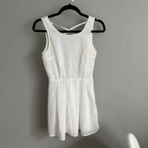 Vit kort klänning Rut&Circle - Superfin vit kort klänning från Rut&Circle i storlek 34. Klänningen har ärmlös design, markerad midja och snygg snörning i ryggen. Tillverkad i ett lätt och luftigt material, med dragkedja i sidan för enkel påklädning. Perfekt för sommarens alla tillfällen!