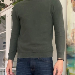 Mörkgrön stickad tröja These Glory Days - Snygg mörkgrön stickad tröja från These Glory Days. Klassisk rund halsringning och ribbade muddar vid ärmslut och nederkant. Perfekt för lager-på-lager och funkar året runt. Enkel och stilren design som passar till jeans eller chinos.