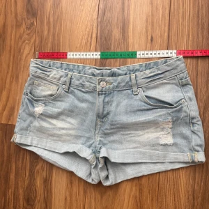 Ljusblå jeansshorts från H&M Divided - Snygga ljusblå jeansshorts från H&M Divided med slitna detaljer framtill och uppvikta kanter. Perfekta för varma dagar och enkel att matcha med allt. Tillverkade i bomull. Storleken i lappen är 40 men hade defenitivt sagt att de motsvarar storlek 38 (M)!!!!! Hör av er vid frågor!