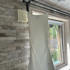 Vit långklänning  - Säljer en stilren   Klänningen är ärmlös med rund halsringning och har en rak, enkel siluett. Perfekt för dig som gillar minimalistisk och clean stil. Materialet är mjukt och följsamt, vilket gör den superbekväm att bära.