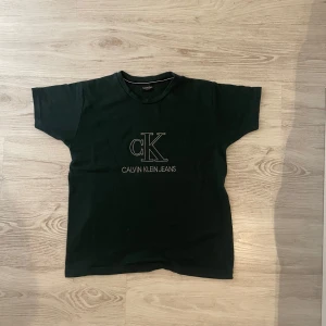 Svart Calvin Klein Jeans t-shirt - Svart t-shirt från Calvin Klein Jeans med broderad CK-logga och text på bröstet. Klassisk rund halsringning och korta ärmar. Tillverkad i mjuk bomull för en skön känsla. Perfekt för en clean och stilren look.